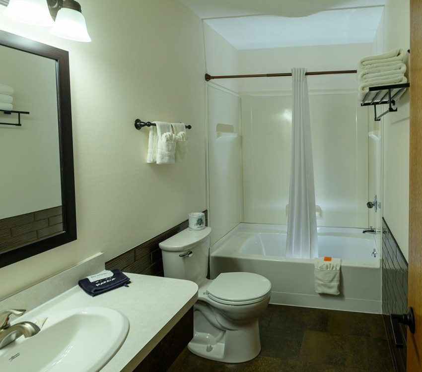 Bathroom with sink, toilet, shower / tub combo, mirror and white walls at Welsh's Motel in Wall, SD
